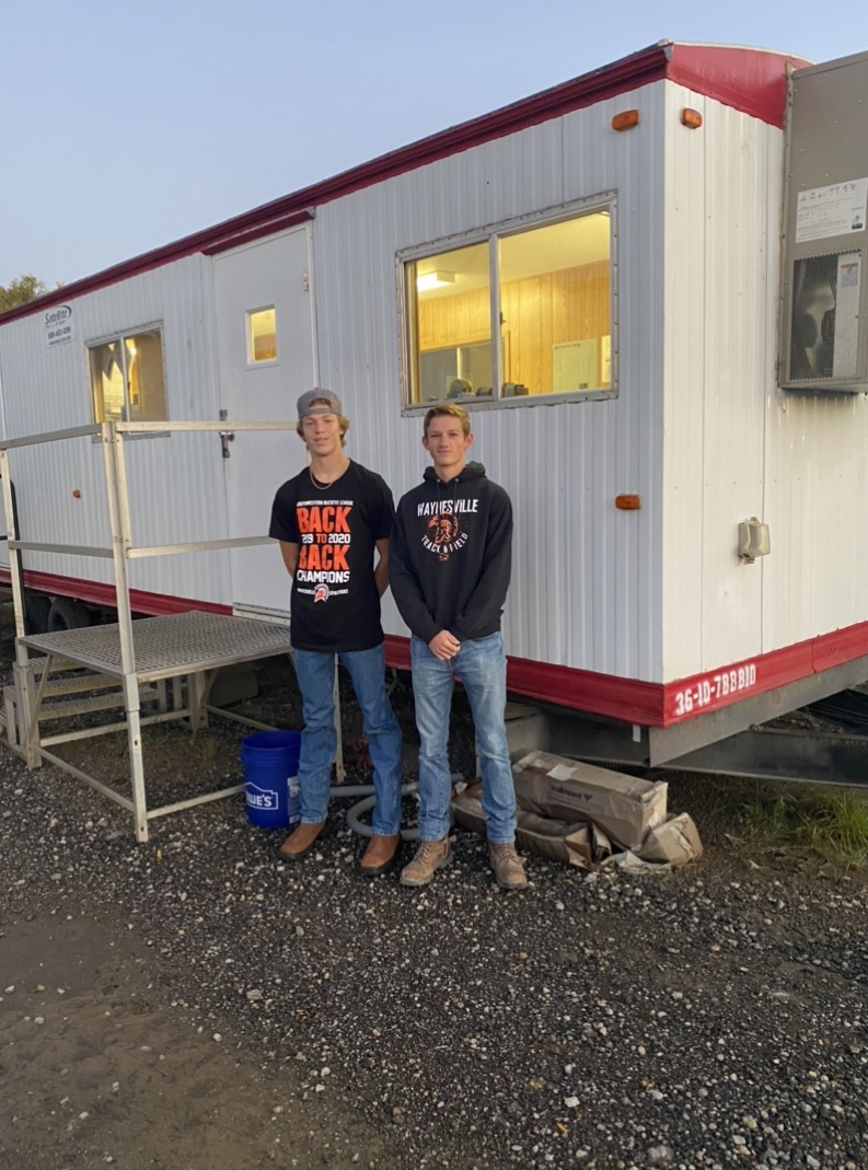 two boys standing in front of a work trailer